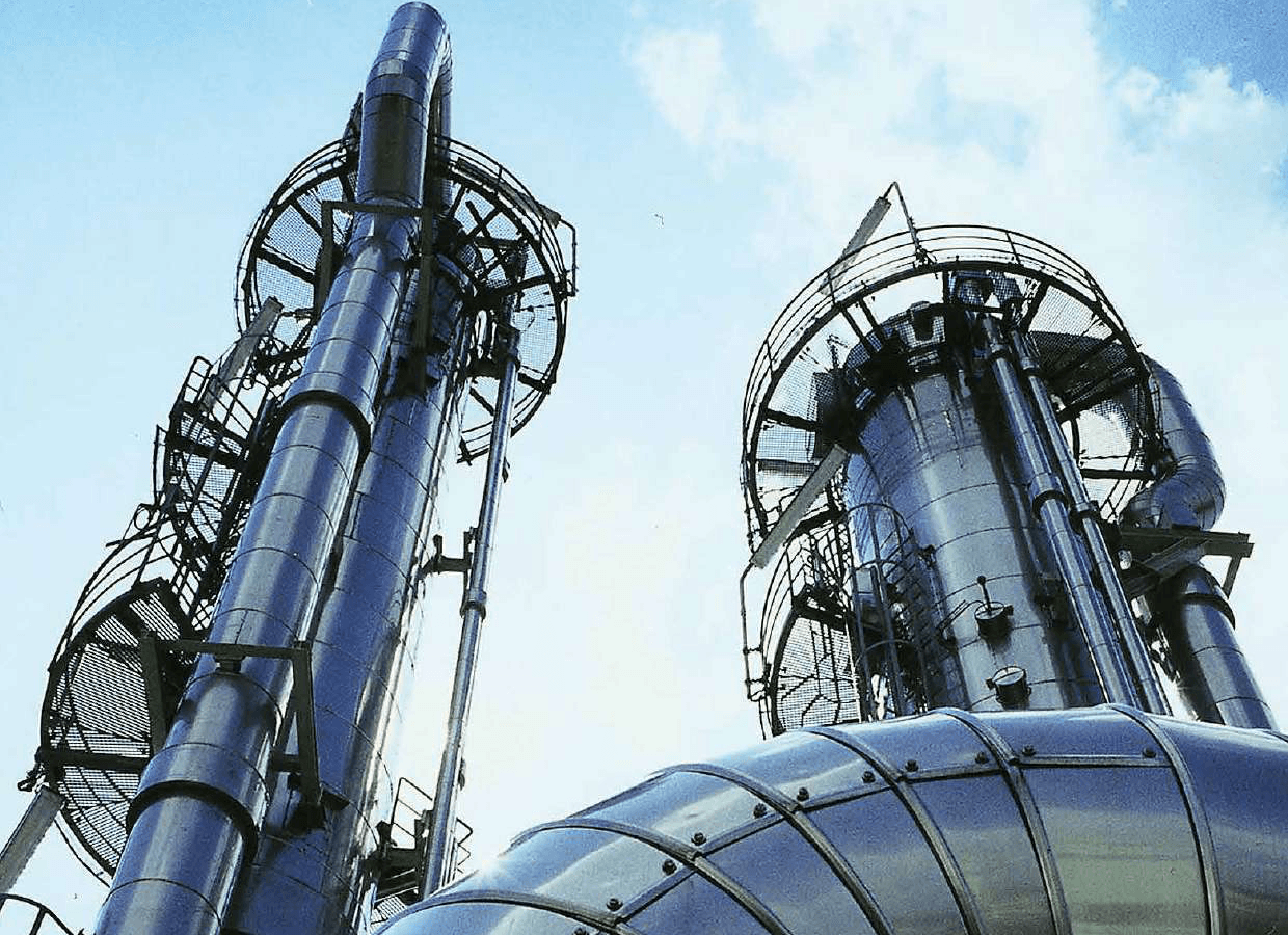 Industrial process towers and piping viewed from below against a clear sky.